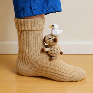 Beige sock with a small crochet capybara and bird toy on a wooden floor.